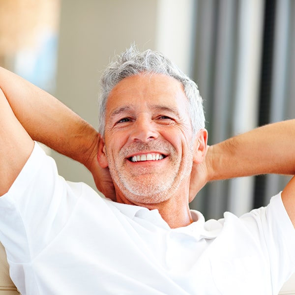 A man is smiling while placing his hands on the back of his neck