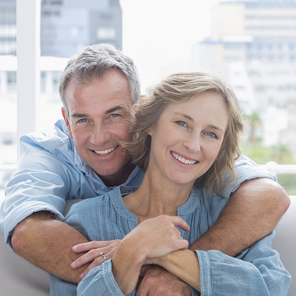 A mature couple hugging and smiling after getting their dental implants